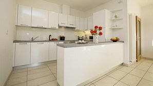 A modern kitchen with white cabinets, a central island, and a vase of red flowers. - Torbole Relax Pool Balcony Apartment (Nago-Torbole)