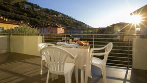 A terrace with a table set for dining, overlooking a hillside with buildings. - Torbole Relax Pool Balcony Apartment (Nago-Torbole)