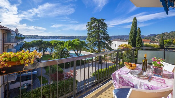 A balcony with a table set for dining, overlooking a scenic view of a body of water and greenery. - Rossella Lake View in Salo (Salò)