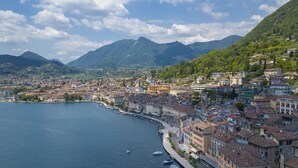 A coastal town with buildings along the waterfront, a marina with boats, and mountains in the background. - Rossella Lake View in Salo (Salò)