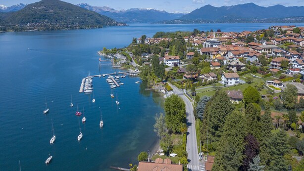 Vue aérienne d’une ville située au bord d’un lac, avec des immeubles résidentiels, un port de plaisance rempli de bateaux et des montagnes en arrière-plan.