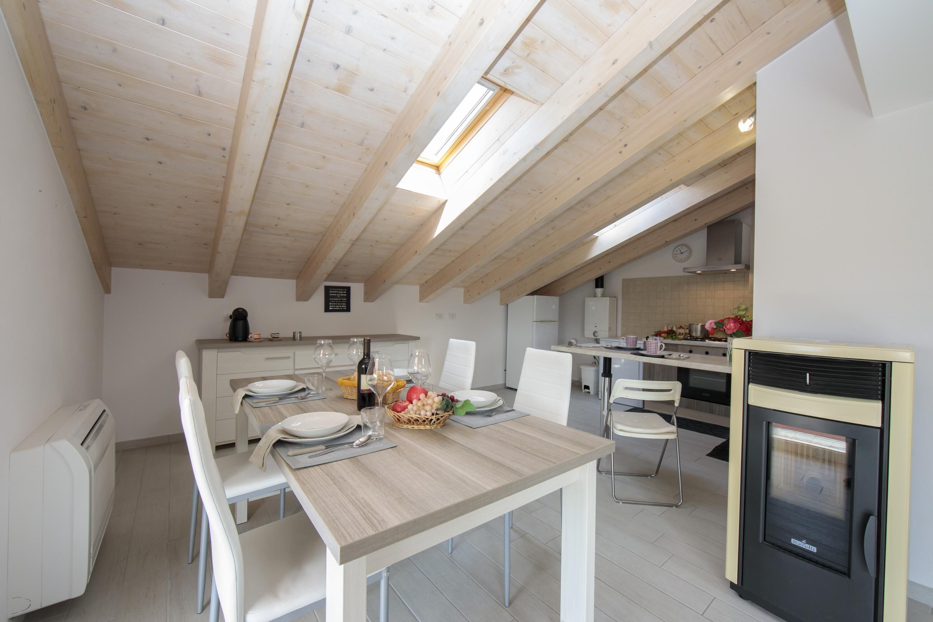 A modern kitchen with wooden beams, a dining area with white chairs, and a built-in oven.