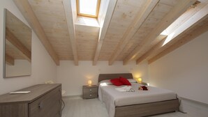 Une chambre avec un puits de lumière, un lit avec des oreillers rouges, une table de chevet avec une lampe et une commode.