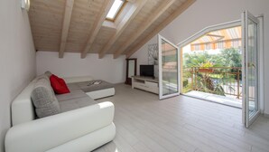 Un salon moderne avec un canapé blanc, un téléviseur à écran plat et un balcon offrant une vue sur la verdure.