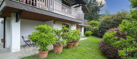A two-story building with a balcony, potted plants, and a stone pathway leading to a door.