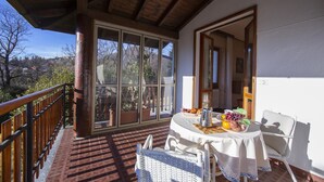 Un balcon abrité avec une table dressée pour le petit-déjeuner, une chaise en osier et une vue sur le paysage environnant.