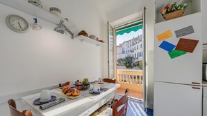 A compact kitchen with a dining table, chairs, a refrigerator, and a window with a view of buildings. - Sunrise Apartment Seaview (Imperia)