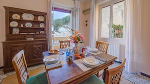 A dining area with a wooden table set for four, a decorative vase with flowers, and a view of the outdoors through a large window. - Sunrise Apartment Seaview (Imperia)