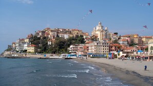 A coastal town with buildings on a hillside, a beach, and a body of water. - Sunrise Apartment Seaview (Imperia)
