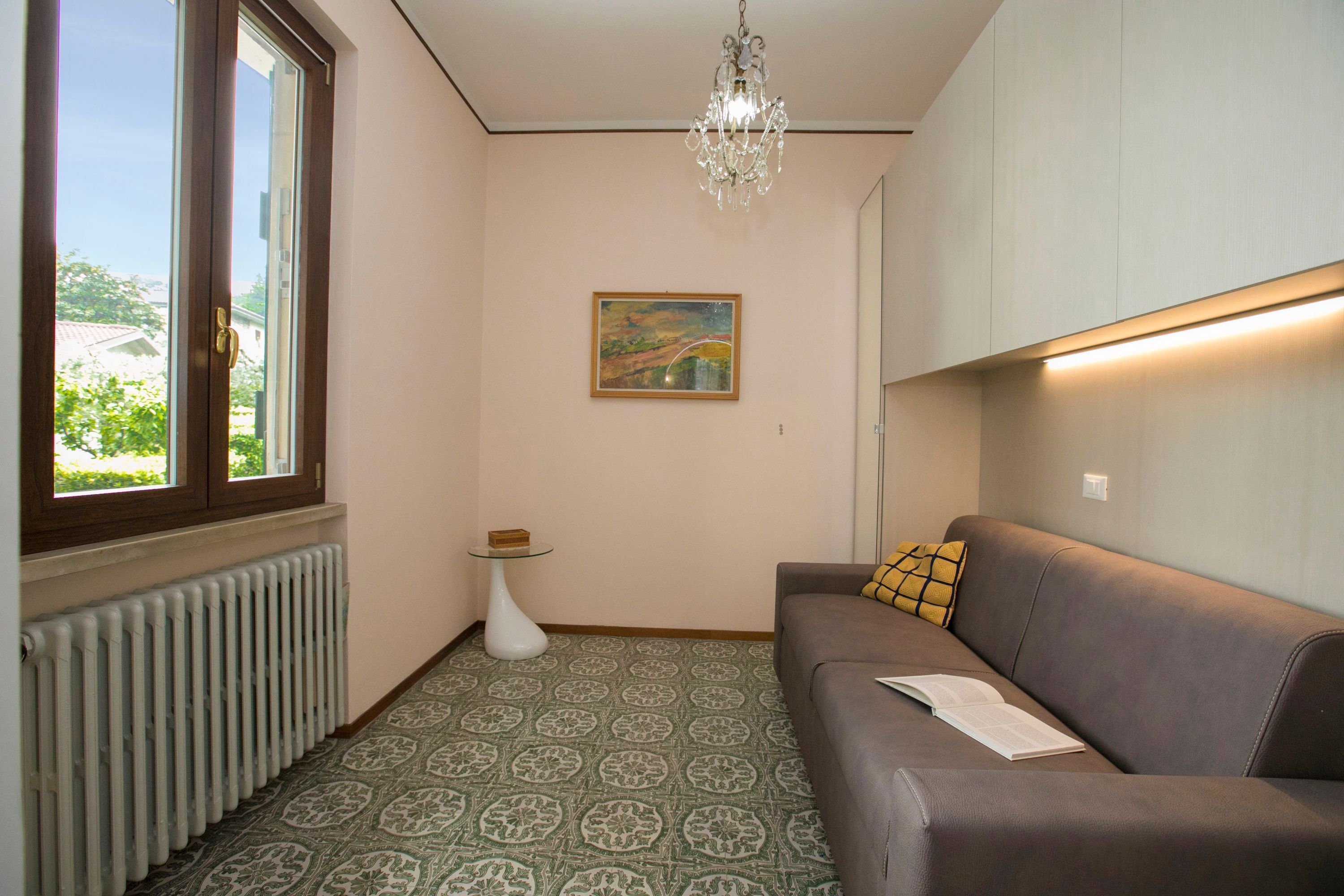 A modern living room with a brown sofa, a small side table, a painting on the wall, and a radiator.