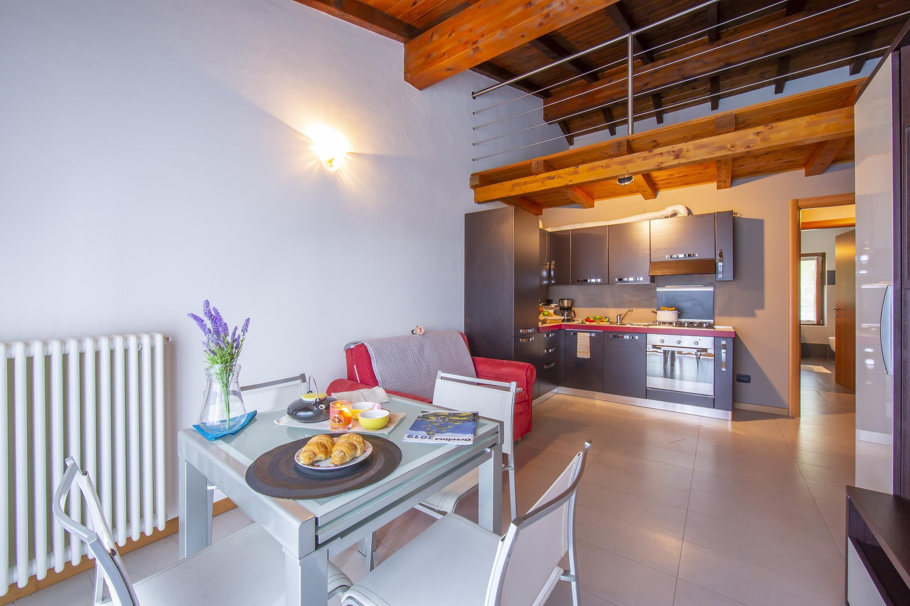 A modern kitchen with built-in appliances, a dining area with a table and chairs, and a red sofa.
