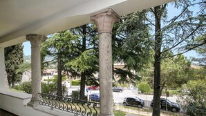 A balcony with stone columns and a wrought iron railing overlooking a street with parked cars and trees. - Villa Alberti Appartamento Bruna (Salò)