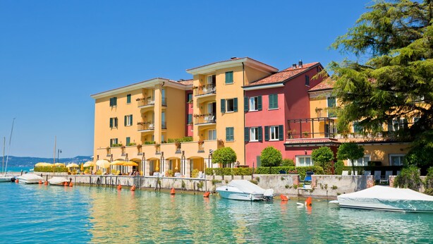 A waterfront hotel with multiple balconies, a marina with boats, and a clear blue sky. - Villa Alberti Appartamento Bruna (Salò)