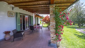 A covered patio with a table and chairs, a stone pillar with climbing plants, and a view of a garden. - Villa Clara few km From the sea (Pietrasanta)