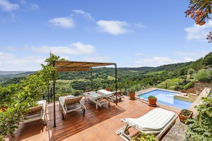 Een terras met lounge stoelen, een zwembad en een prachtig uitzicht op glooiende heuvels.
