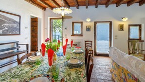 A dining area with a wooden ceiling, a table set with plates, glasses, and a vase of flowers. There are chairs around the table, and a bench is visible in the background. - Villa Formaga in Hilly Area Relax and vie (Gargnano)