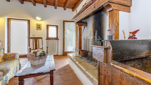 A rustic interior with a stone fireplace, wooden beams, a wicker basket on a table, and a bed with floral bedding. - Villa Formaga in Hilly Area Relax and vie (Gargnano)