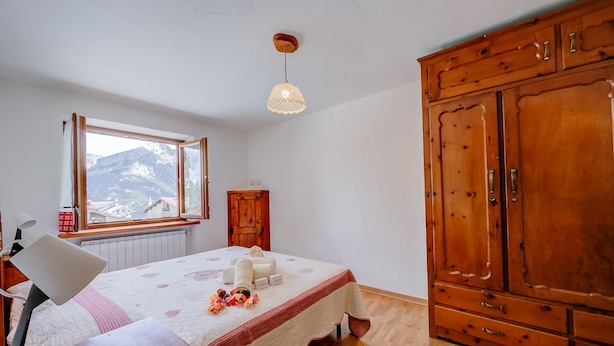 A bedroom with a large wooden wardrobe, a bed with a mountain view through the window, and a desk with a lamp. - Miramonti 21 Ski In - Ski Out (Sauze d'Oulx)