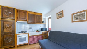 A compact kitchen with wooden cabinets, a white countertop, and a grey sofa. - Miramonti 21 Ski In - Ski Out (Sauze d'Oulx)