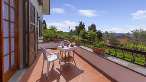 A balcony with a table and chairs, potted plants, and a view of greenery and buildings. - Villino di Corsanico With View (Massarosa)