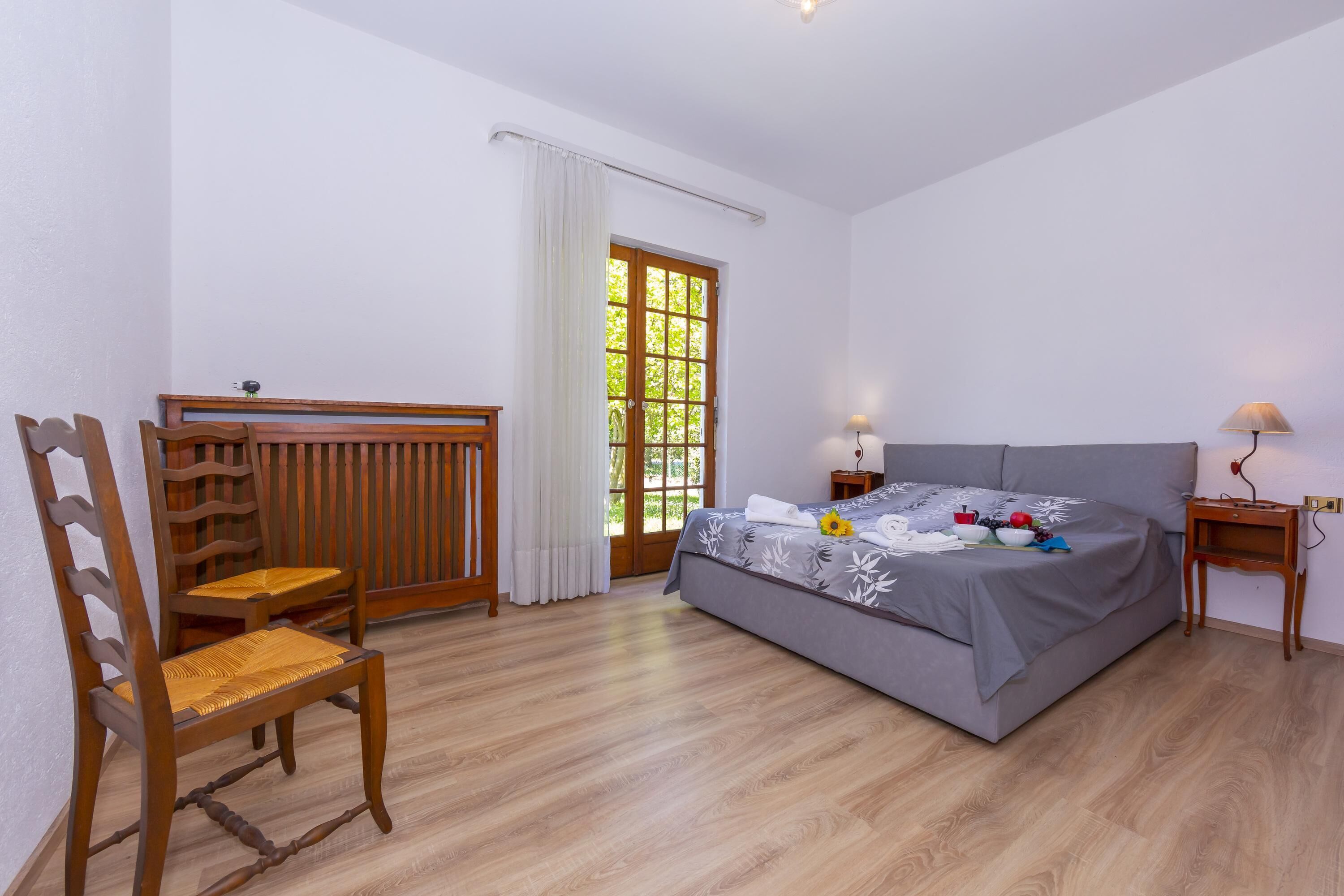 A bedroom with a bed, a chair, a nightstand, and a window with curtains.