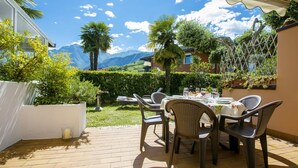 Un patio al aire libre con una mesa lista para comer, rodeada de sillas, y vistas a montañas al fondo.