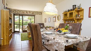 Un comedor con una mesa dispuesta para cuatro, sillas, una estantería de madera y vistas a un jardín a través de un ventanal.