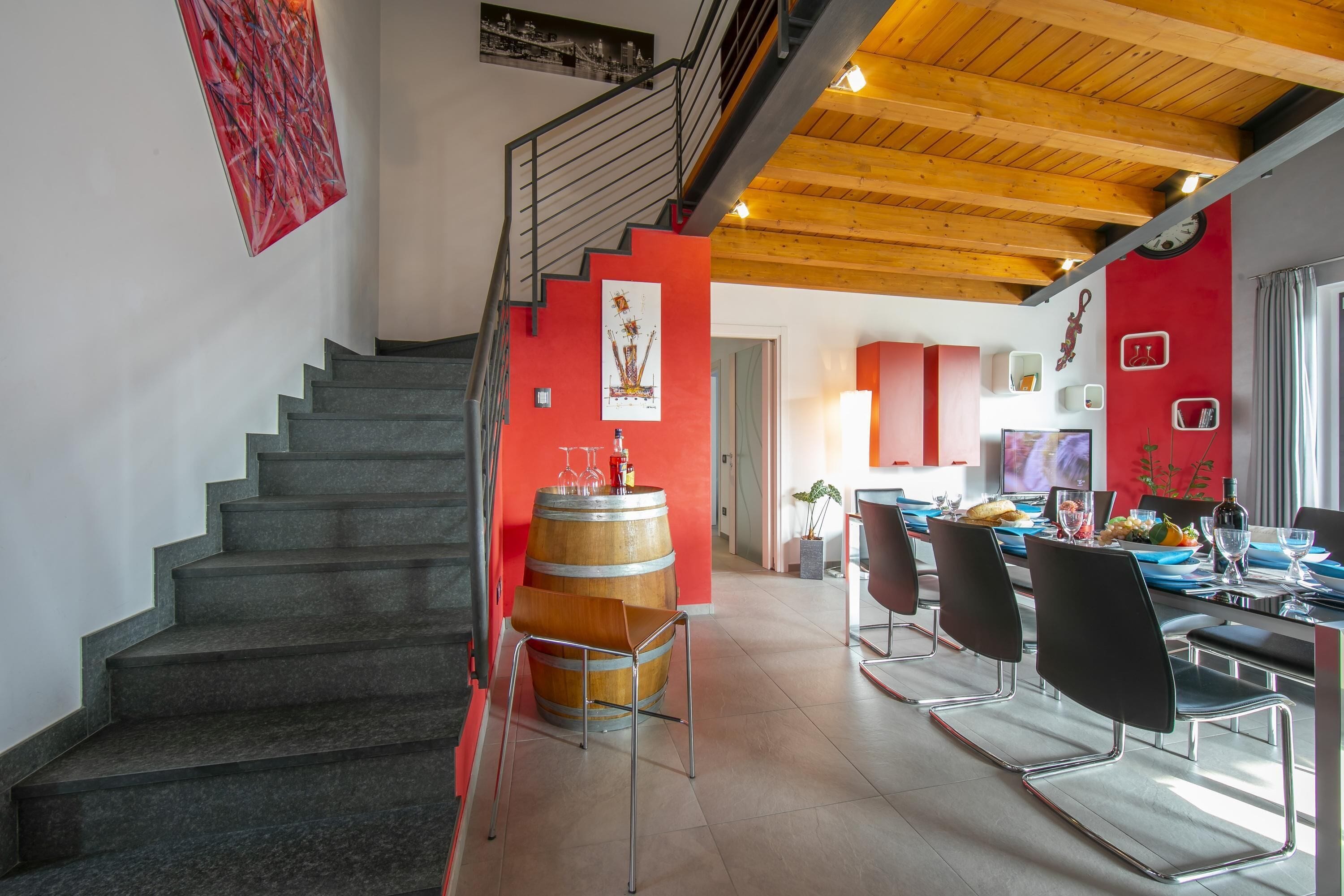 A modern interior with a staircase, a dining area with a wooden barrel centerpiece, and a kitchen visible in the background.