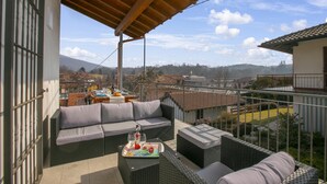Un balcón con mobiliario de mimbre, una mesa con una bandeja de bebidas y vistas a un pueblo y montañas.