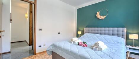 A bedroom with a large bed, a teal accent wall, and a wooden herringbone floor.