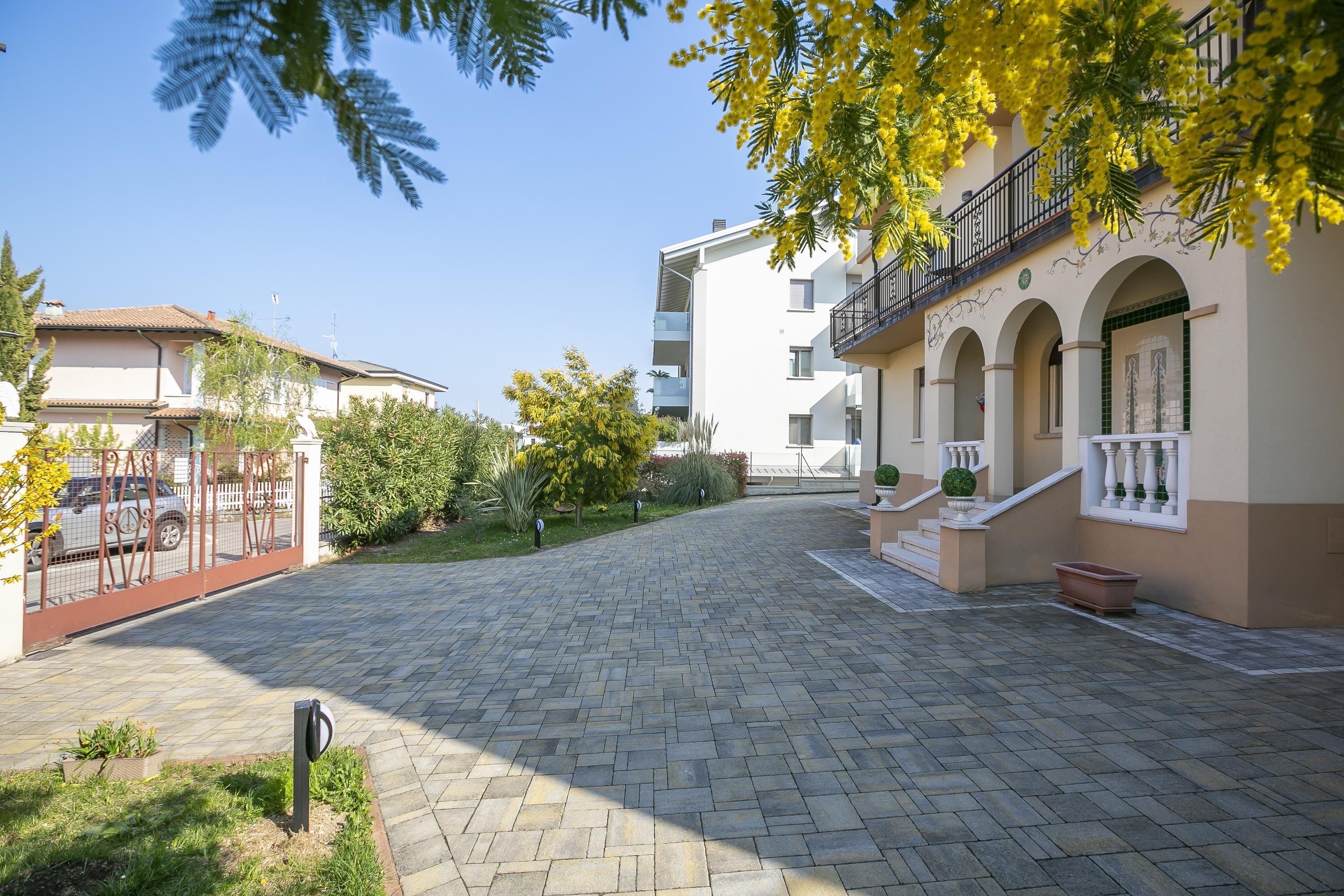 A courtyard with a paved walkway, a gated entrance, and a building with balconies and arched windows.