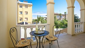 A balcony with two chairs, a table with a bottle and glasses, and a view of buildings and greenery. - Villa Mimosa - Appartamento 1 (Desenzano del Garda)