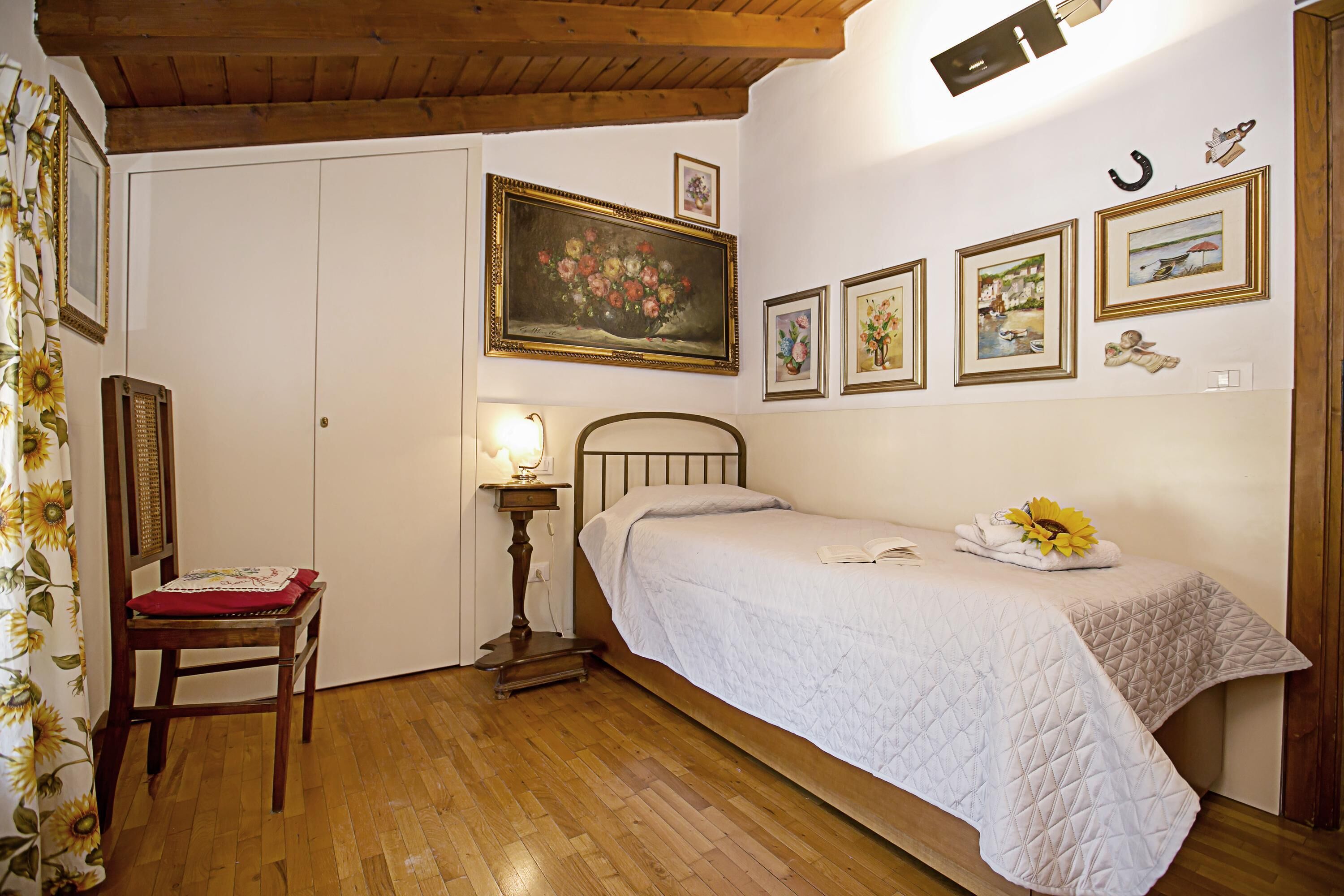 Ein Schlafzimmer mit einem Bett, einem Sessel, einem Nachttisch mit Lampe und einer Wand mit gerahmten Bildern.