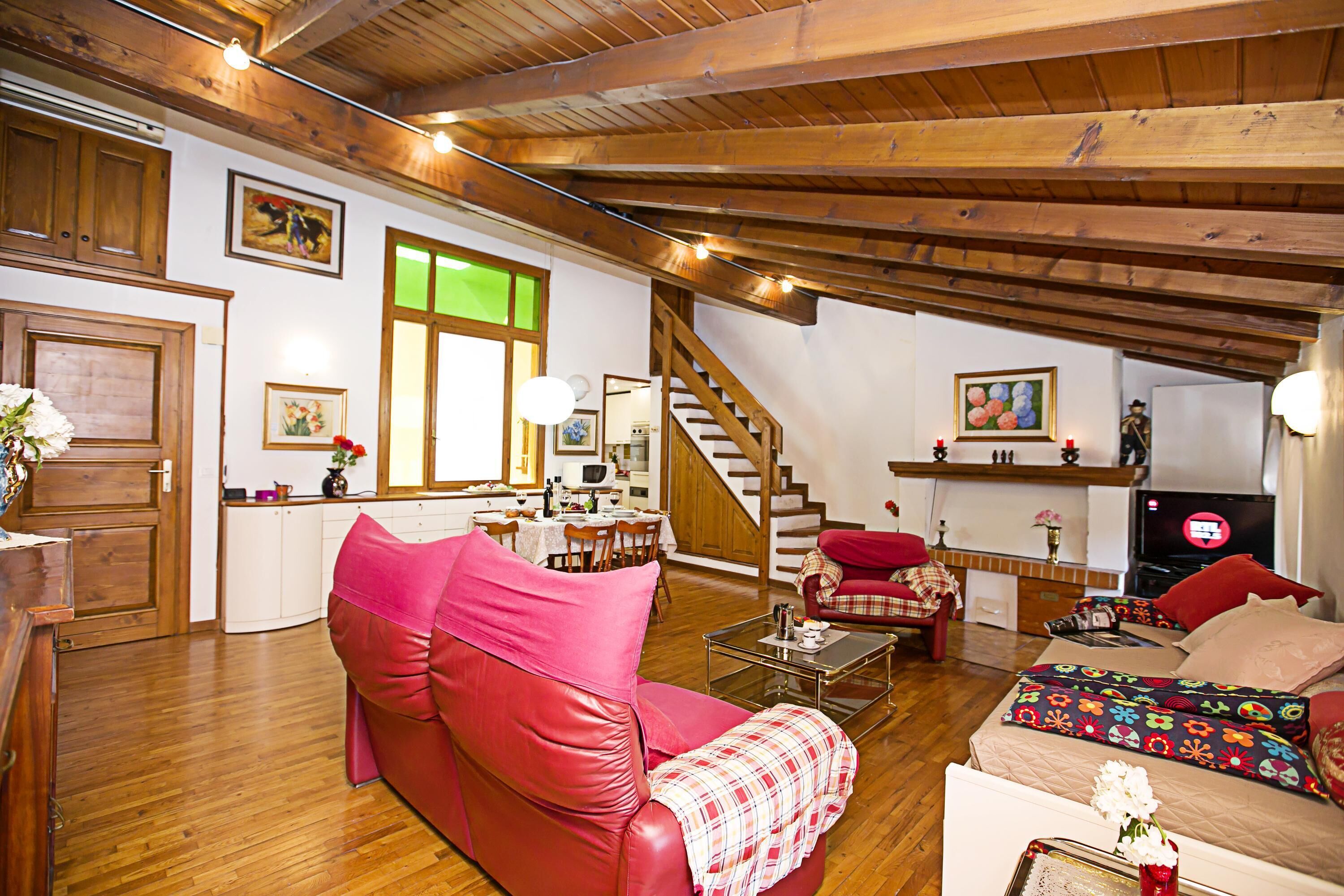 Ein gemütliches Wohnzimmer mit einem roten Sofa, einem Couchtisch und einem Fernseher. Eine Treppe führt zu einer oberen Ebene.
