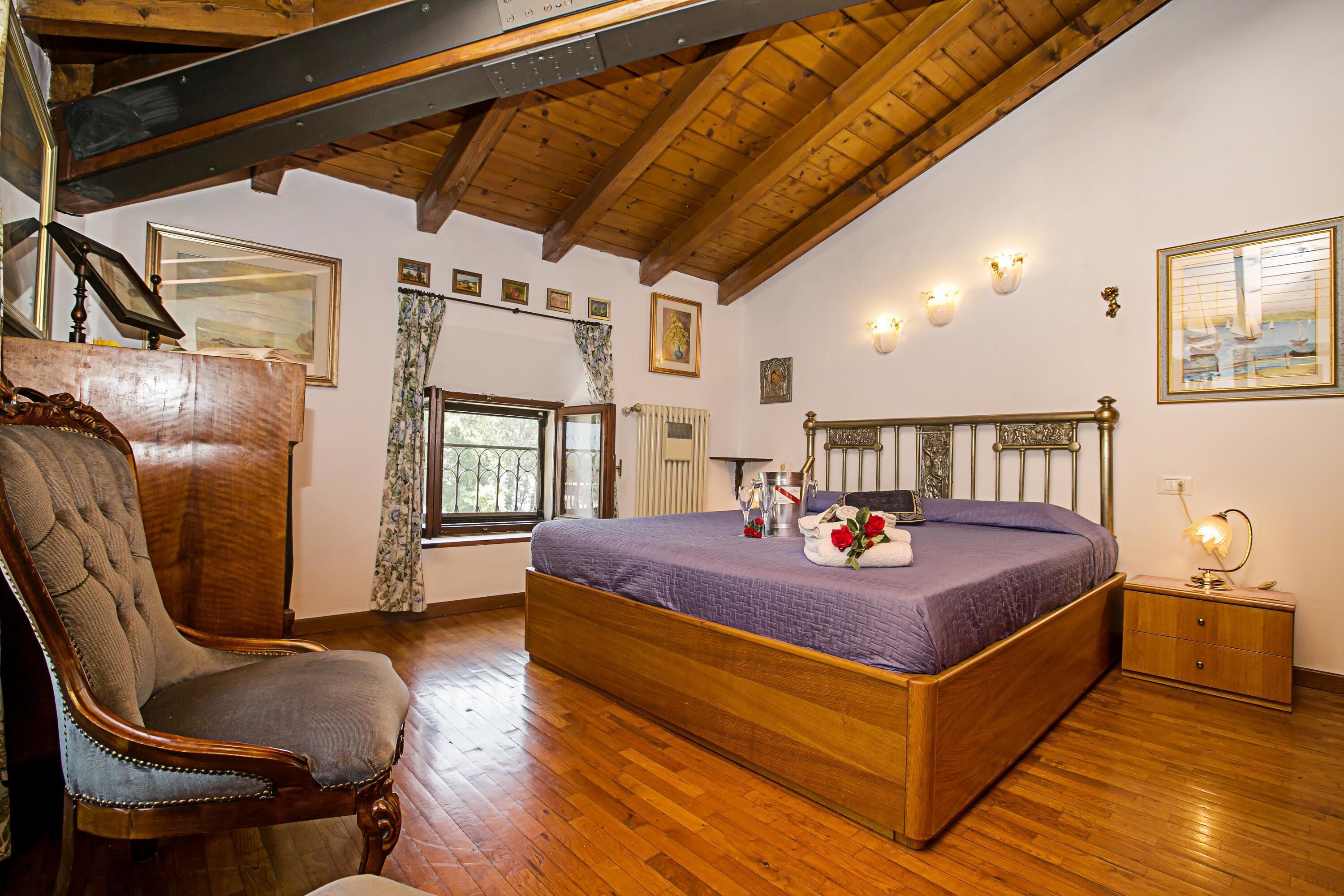 A bedroom with a wooden bed, a large chair, a nightstand, and a window with curtains.