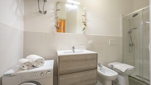 Ein modernes Badezimmer mit Waschmaschine, Waschbecken, Bidet und einer Duschkabine.
