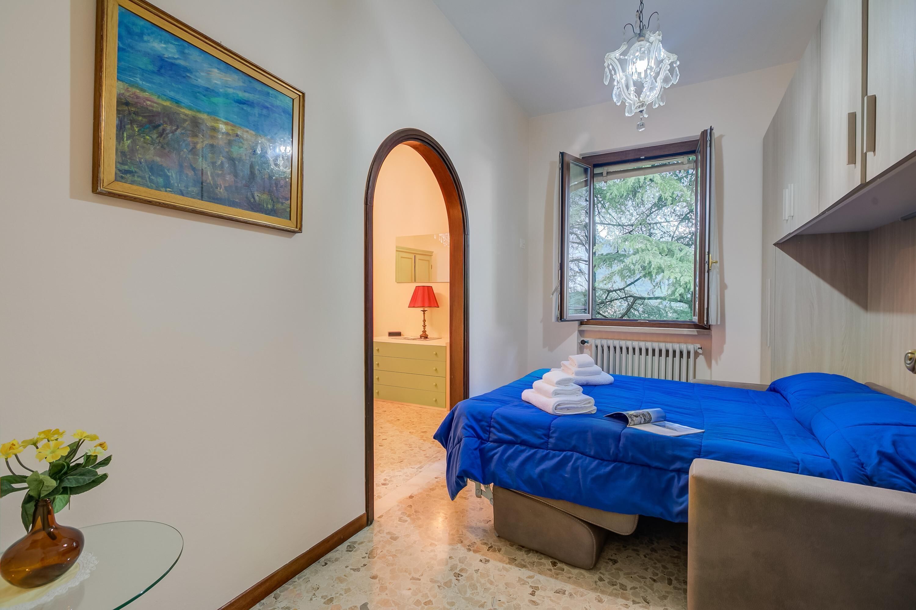 Une chambre à coucher avec un lit, une fenêtre, un tableau et un vase de fleurs.