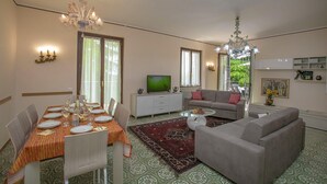 A dining area with a table set for four, a sofa, a television, and a chandelier. - Villa Alberti 900m From Garda Lake (Salò)