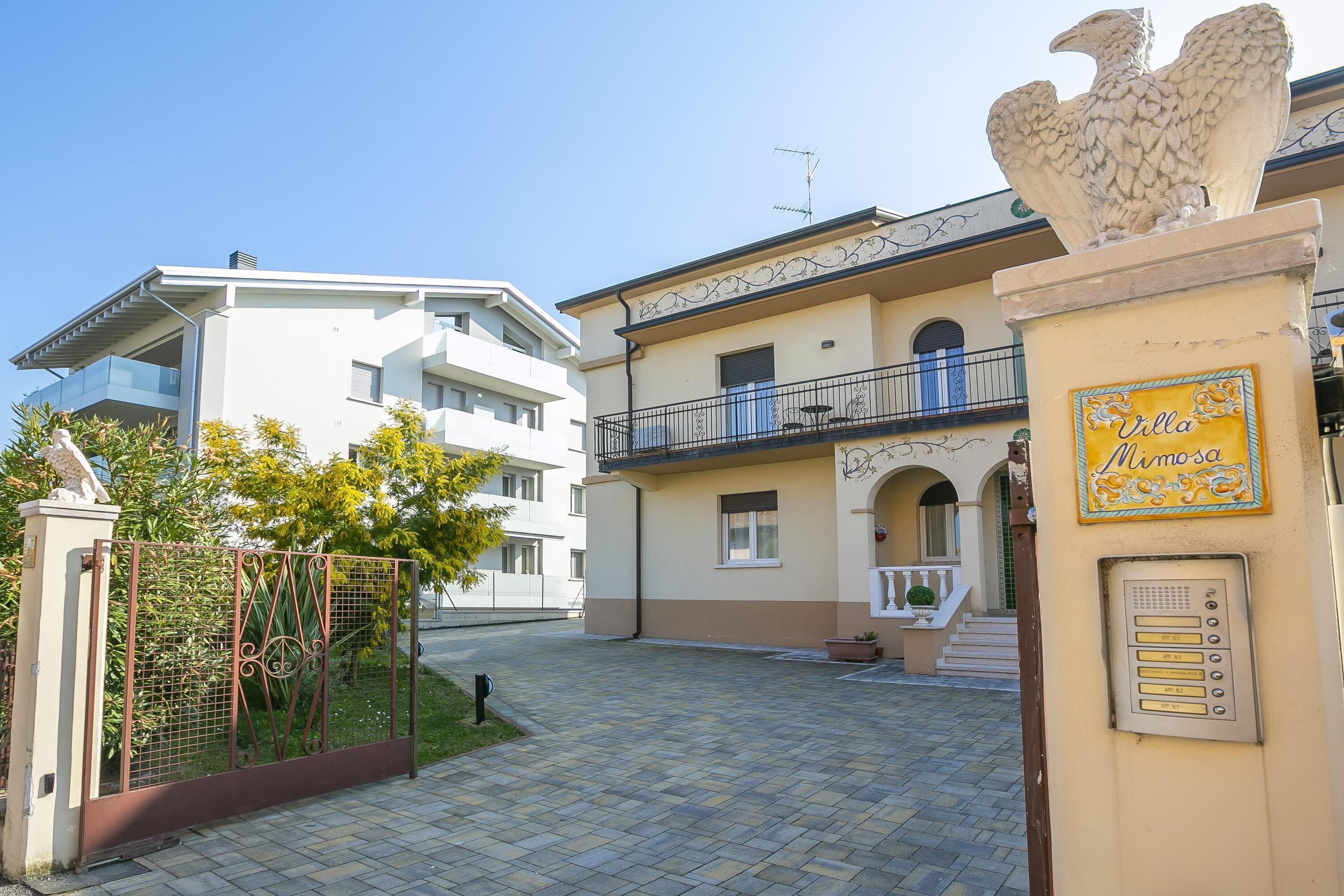 A gated courtyard with a building featuring a balcony and a plaque reading "Villa Mimoza."