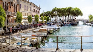 Un canale con imbarcazioni ormeggiate, un ponte e edifici con tavoli all'aperto.