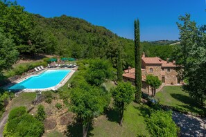 A large swimming pool surrounded by lush greenery and a stone building with a tiled roof. - Villa Casacheta in Montaione (Montaione)
