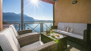 A balcony with wicker furniture, a white sofa, and a table with a plant and a bottle. - Panorama Fantastico Apt Pool Beach (Ghiffa)