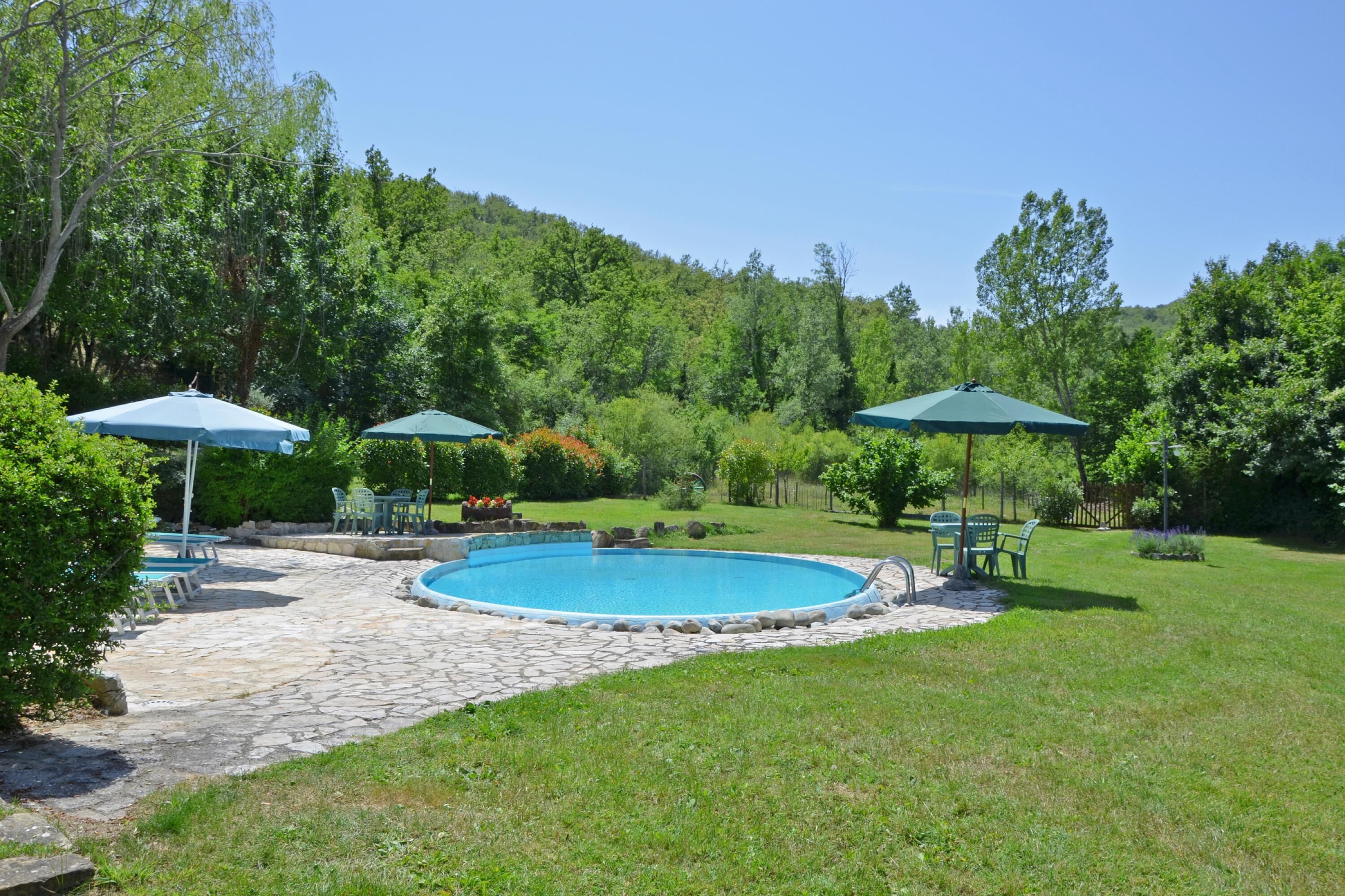 A backyard with a swimming pool, stone patio, and green umbrellas.