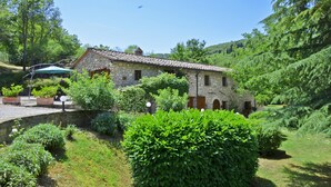 A stone building with a tiled roof, surrounded by lush greenery and a small pond. - Molino del Ponte in Radda in Chianti (Radda in Chianti)