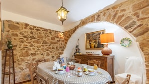 Un comedor con pared de piedra, una mesa redonda dispuesta con platos, tazas y una lámpara.
