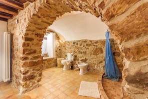 Un baño rústico con paredes de piedra, suelo de baldosas y techo de madera.