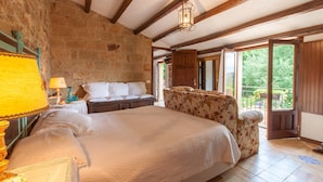 Un dormitorio con una cama grande, un sillón floral, techo de madera y vistas al exterior.