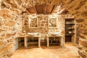 Un baño rústico con paredes de piedra, vigas de madera y dos lavamanos grandes con espejos.