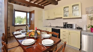 A dining area with a wooden table set for four, a kitchen with light-colored cabinets, and a view through a window.