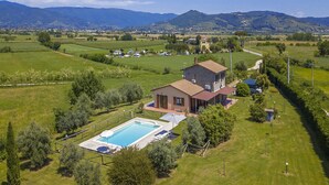 A house with a swimming pool, surrounded by green fields and mountains in the background.